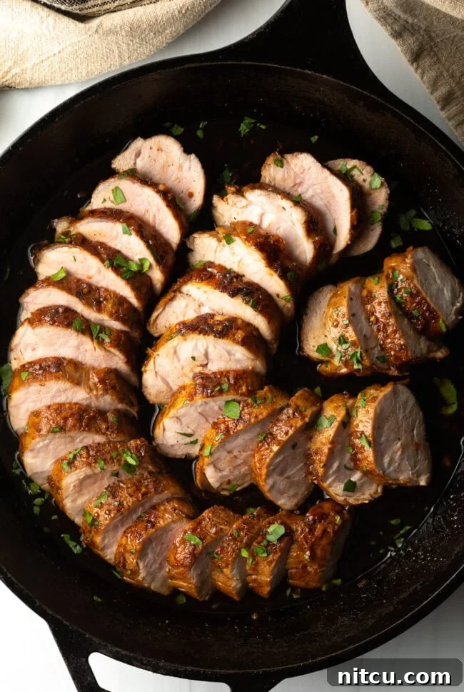 Top-down view of succulent slices of roasted honey garlic pork tenderloin, arranged artfully in a sleek black cast iron pan, showcasing the delicious glaze.