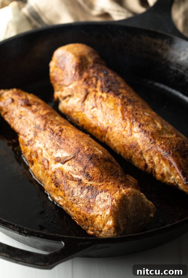 Two perfectly seared pork tenderloins, golden brown and ready for the next step, resting in a black cast iron skillet.