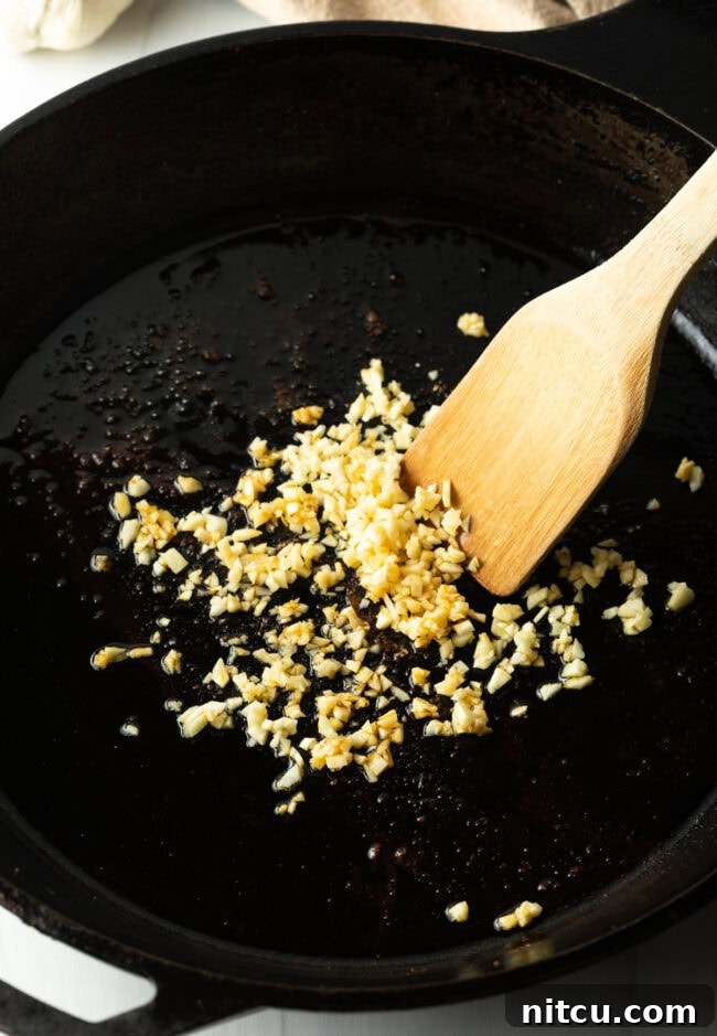 Freshly minced garlic sizzling and sautéing in a hot cast iron skillet, being stirred with a wooden spatula.