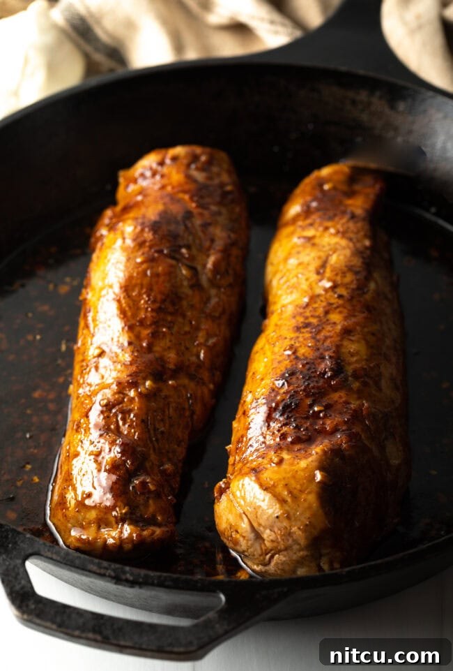 Two oven-roasted pork tenderloins, beautifully glazed and browned, nestled back into a cast iron skillet.