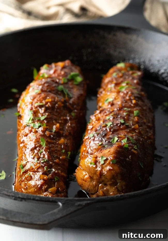Two oven-roasted pork tenderloins with a sticky honey garlic glaze, showcased in a black cast iron skillet, ready to be sliced.