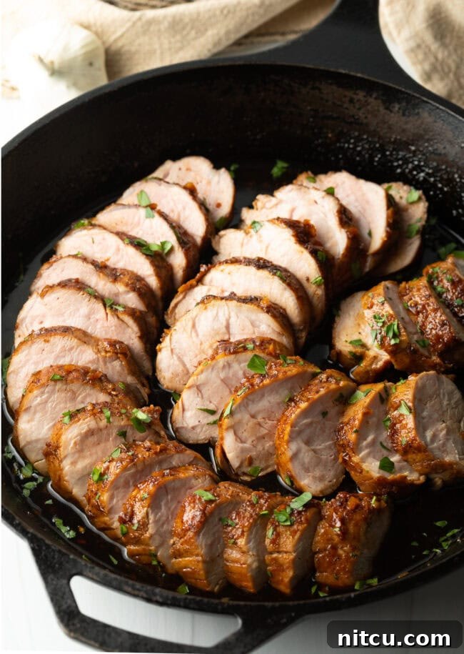 Tender slices of slow cooker honey garlic pork tenderloin, glistening with sauce, artfully arranged in a black cast iron pan.