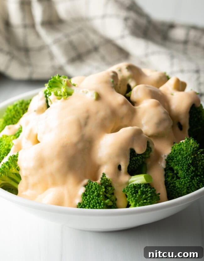 Bowl of steamed broccoli florets covered in homemade cheddar cheese sauce.