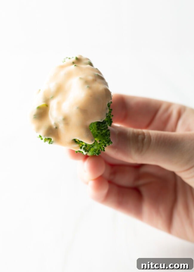 Hand holding broccoli floret coated with cheese sauce for broccoli to camera.