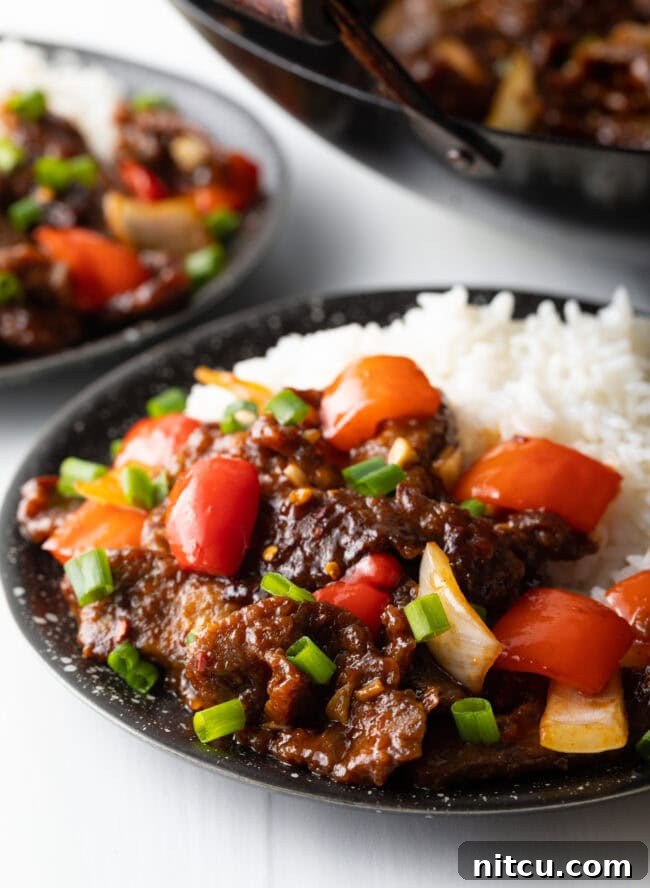Beijing Beef with rice in a black bowl, garnished with scallions.