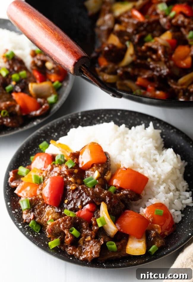Side view Beijing beef in a black bowl with rice.