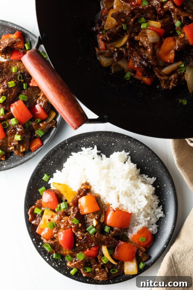 Top down view Beijing beef in a bowl with rice next to a skillet with remaining beef.
