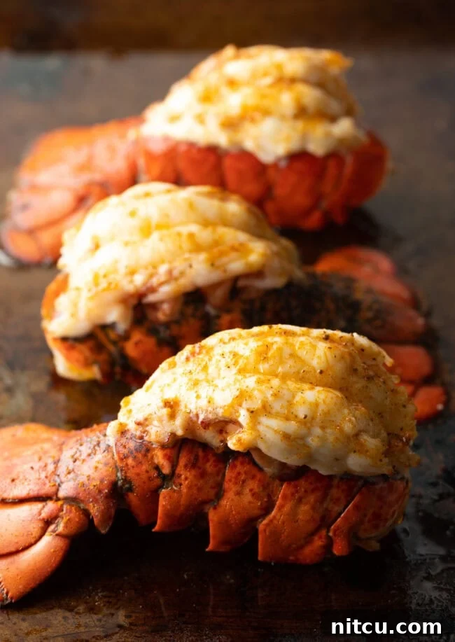 Three plump cooked lobster tails on a baking sheet, glistening with butter.