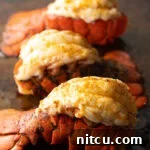 Three plump cooked lobster tails on a baking sheet.