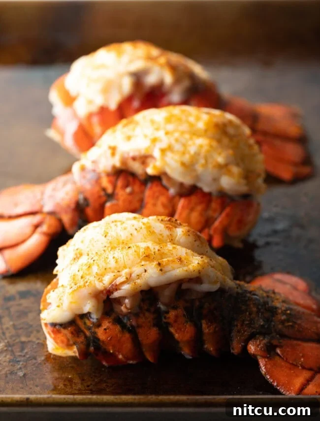 Three perfectly baked lobster tails, plump and glistening with butter, arranged on a baking sheet, ready to be served.
