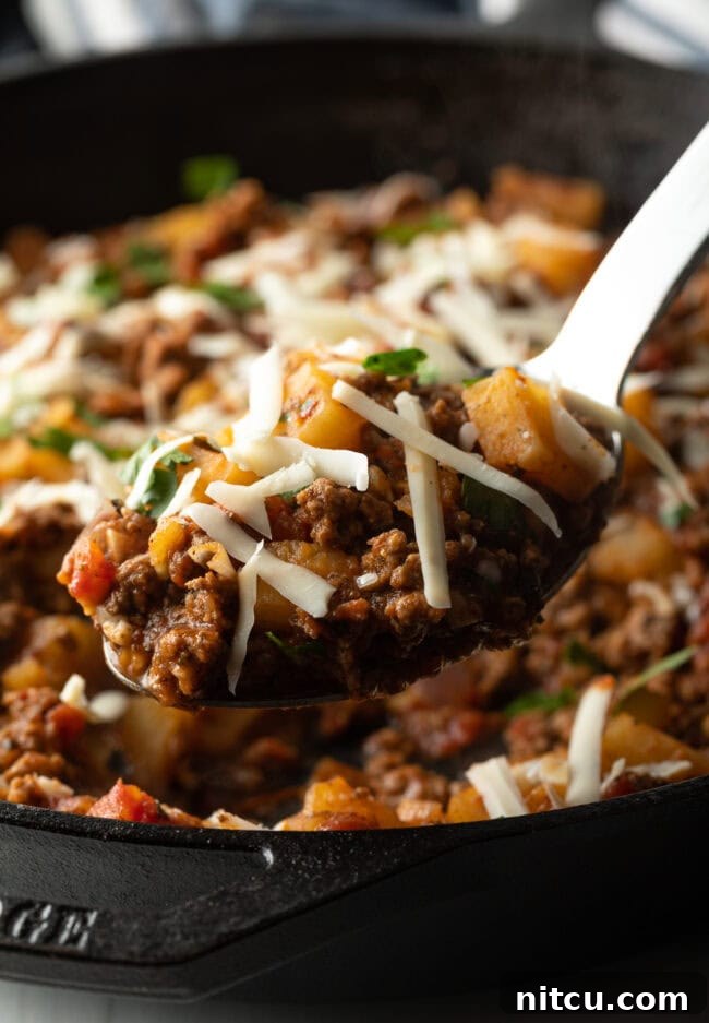 Metal spoon with potatoes and ground meat, topped with shredded parmesan cheese.