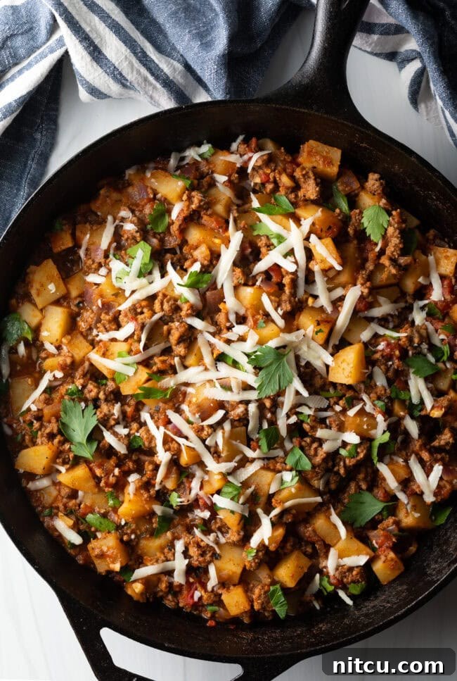 Top down view ground beef and potatoes, topped with shredded parmesan cheese in a skillet.