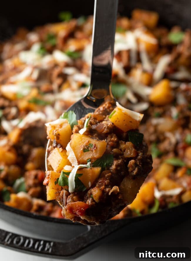 Metal spoon with ground beef and potatoes, topped with shredded parmesan cheese.