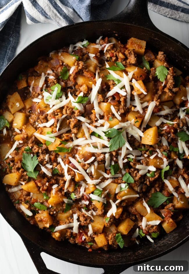 Top down view ground beef and potatoes, topped with shredded parmesan cheese in a skillet.