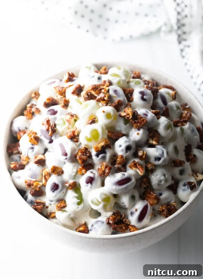 Grape salad in a white bowl, topped with crunchy chopped pecans.