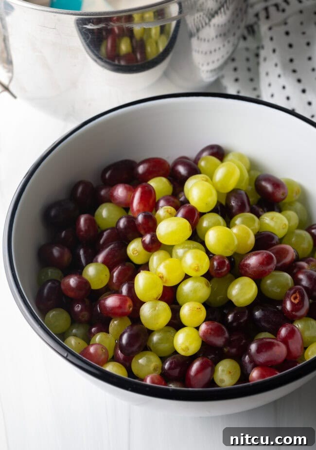 Green and red grapes, removed from the stems, in a white bowl.