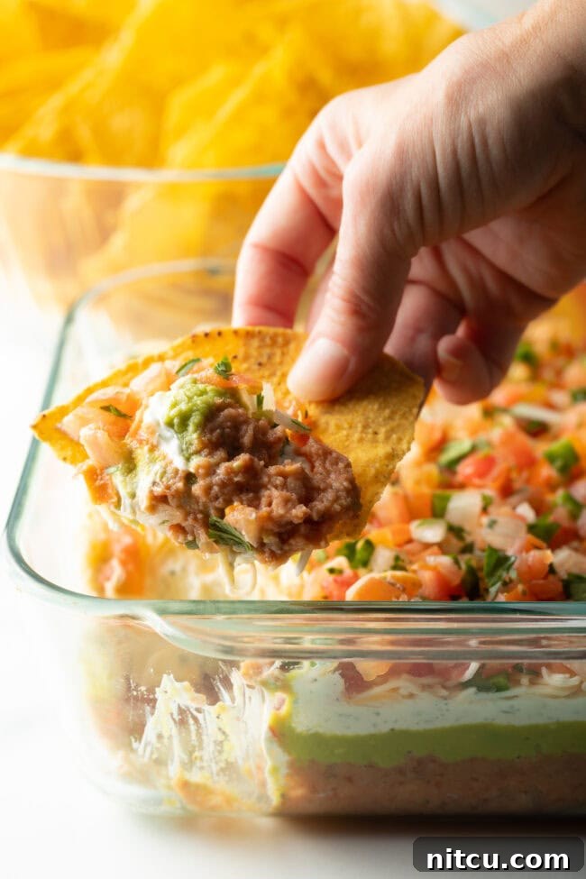 Close view of tortilla with a hand using a chip to scoop the 5 layer bean dip.