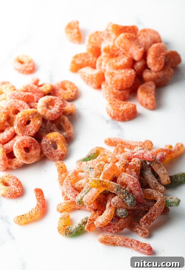 Top down view of four piles of chamoy and tajin coated gummy candies, glistening and ready to eat.