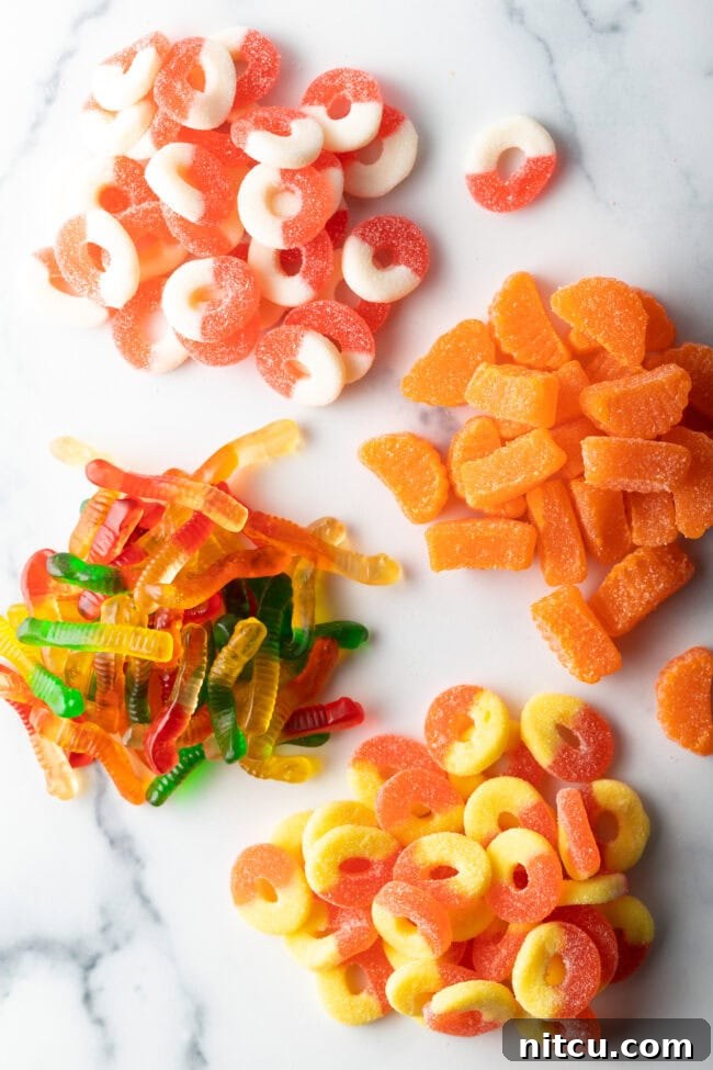 Top down view of four piles of different gummy candies: White and orange circles, orange slices, yellow and orange circles, before coating.
