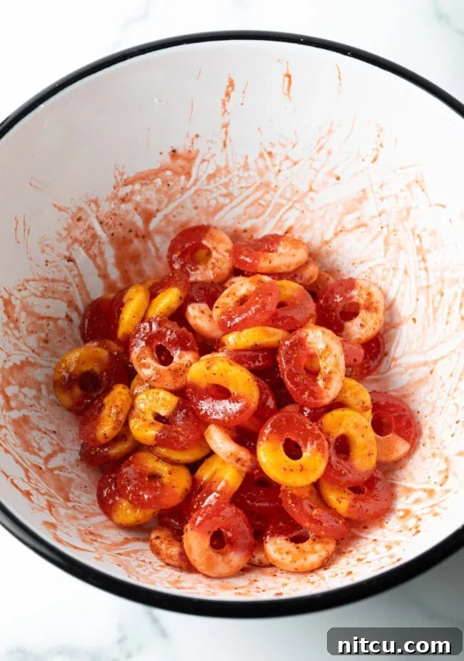 Gummy fruit rings tossed in sauce and seasoning in a white bowl, glistening and ready for drying.