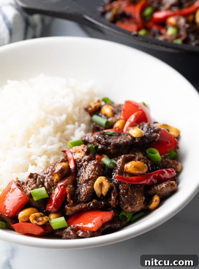 A large serving of Kung Pao beef stir fry in a white bowl with white rice, ready to be eaten.