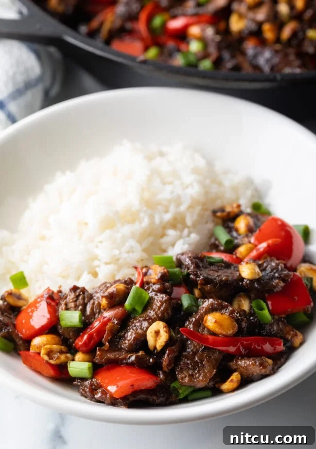A close-up of Kung Pao beef stir fry in a white bowl with white rice, showing the glossy sauce and ingredients.