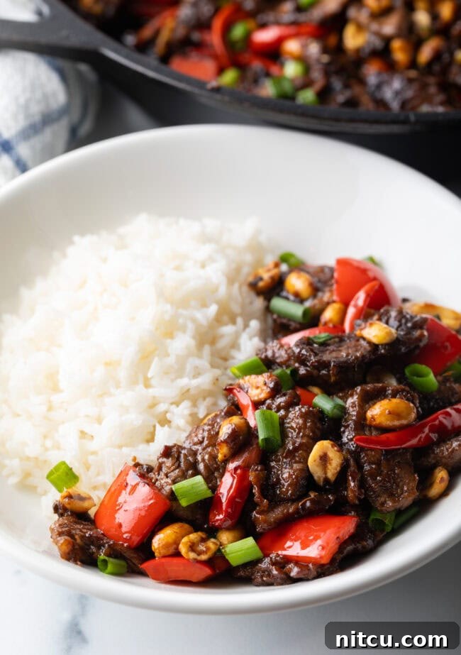 A perfectly cooked Kung Pao beef stir fry, garnished, served in a white bowl with rice.