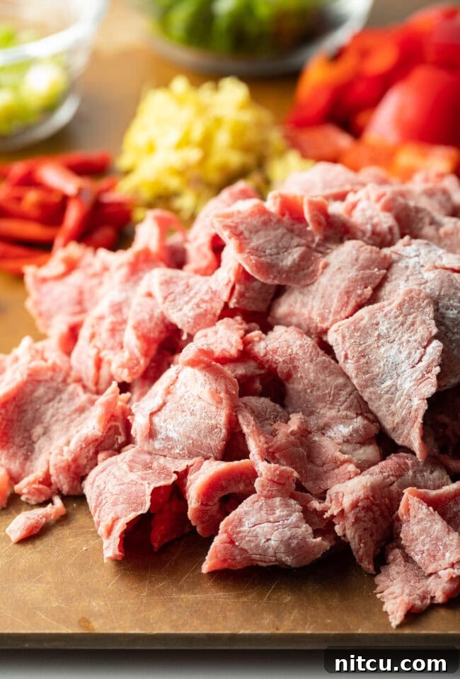 Recipe ingredients chopped on a cutting board in individual piles: steak, onion, red bell peppers, garlic, ginger, and chilies.