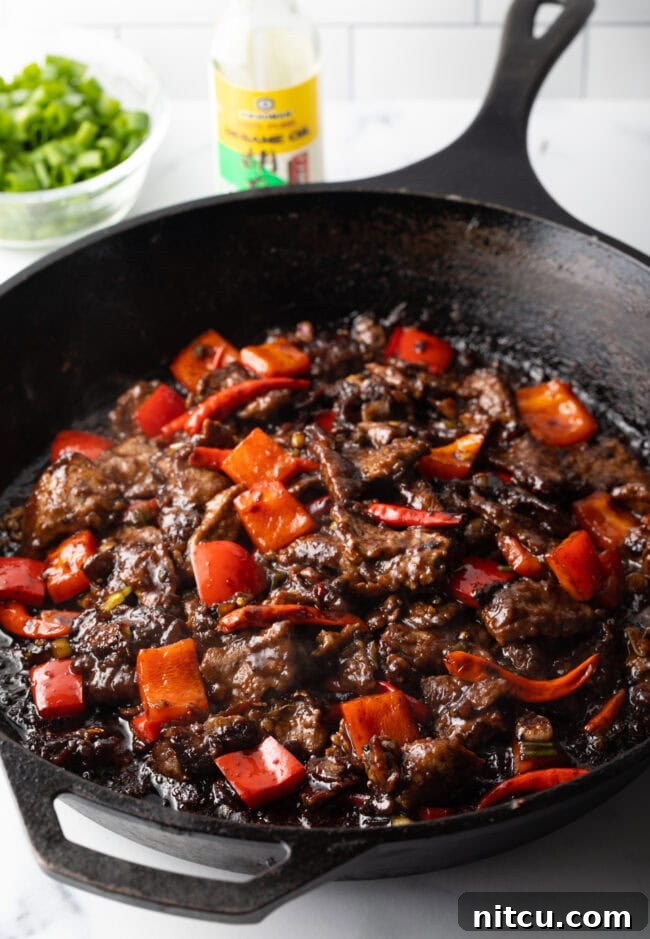 Chopped steak and bell peppers being stir-fried in a skillet, mid-cooking.
