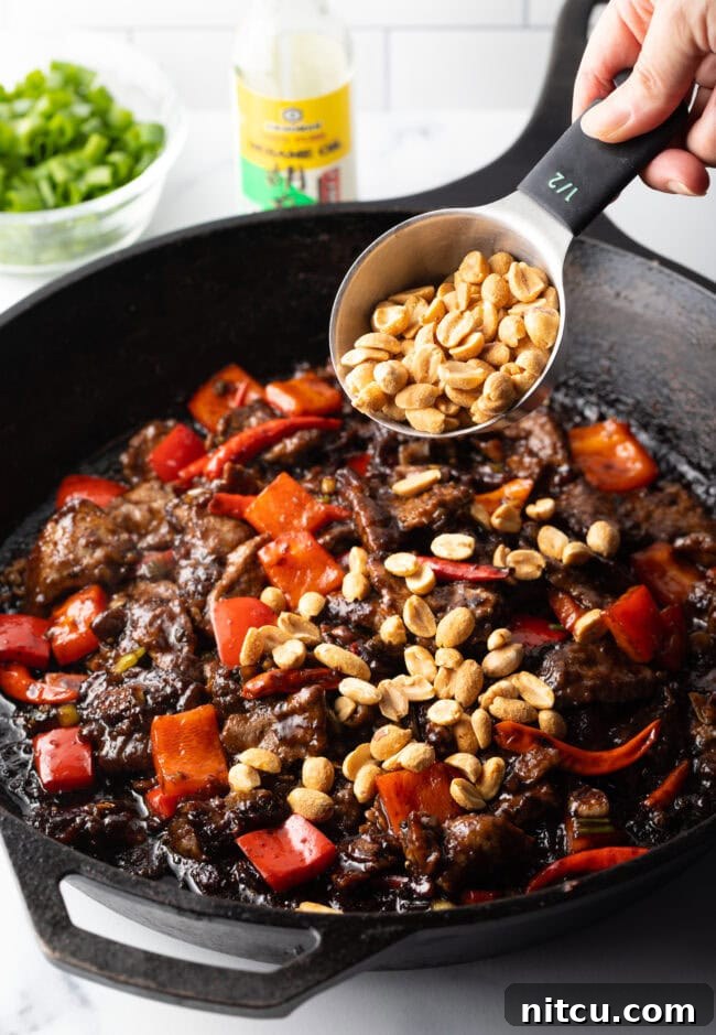 A hand adding chopped peanuts into the skillet with the stir-fry.