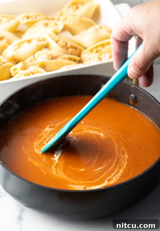 Hand with blue spatula stirring cheese mixture in a saucepan.