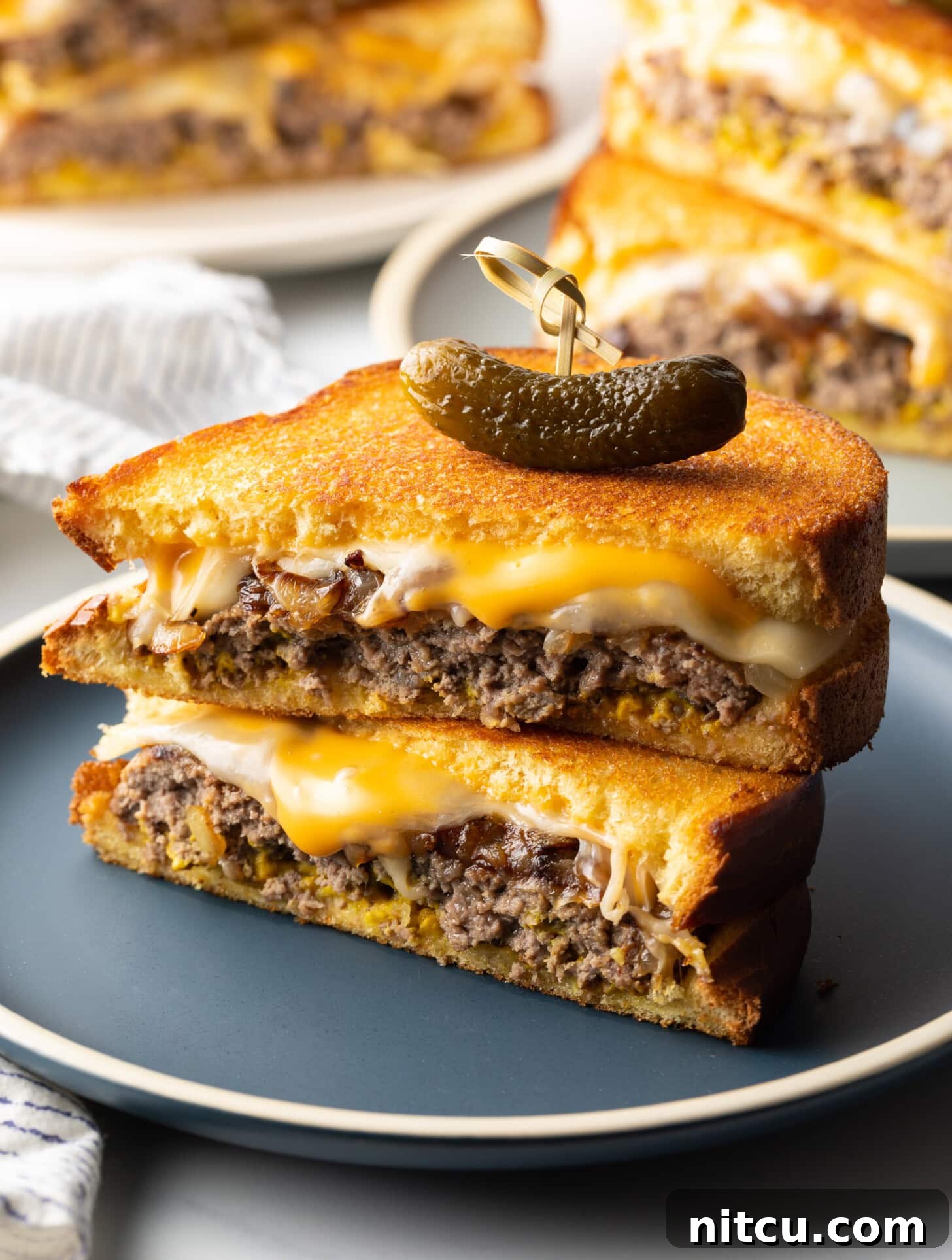 Two halves of a patty melt stacked on top of each other. A wood skewer with small pickle is going through the top of the sandwich stack.
