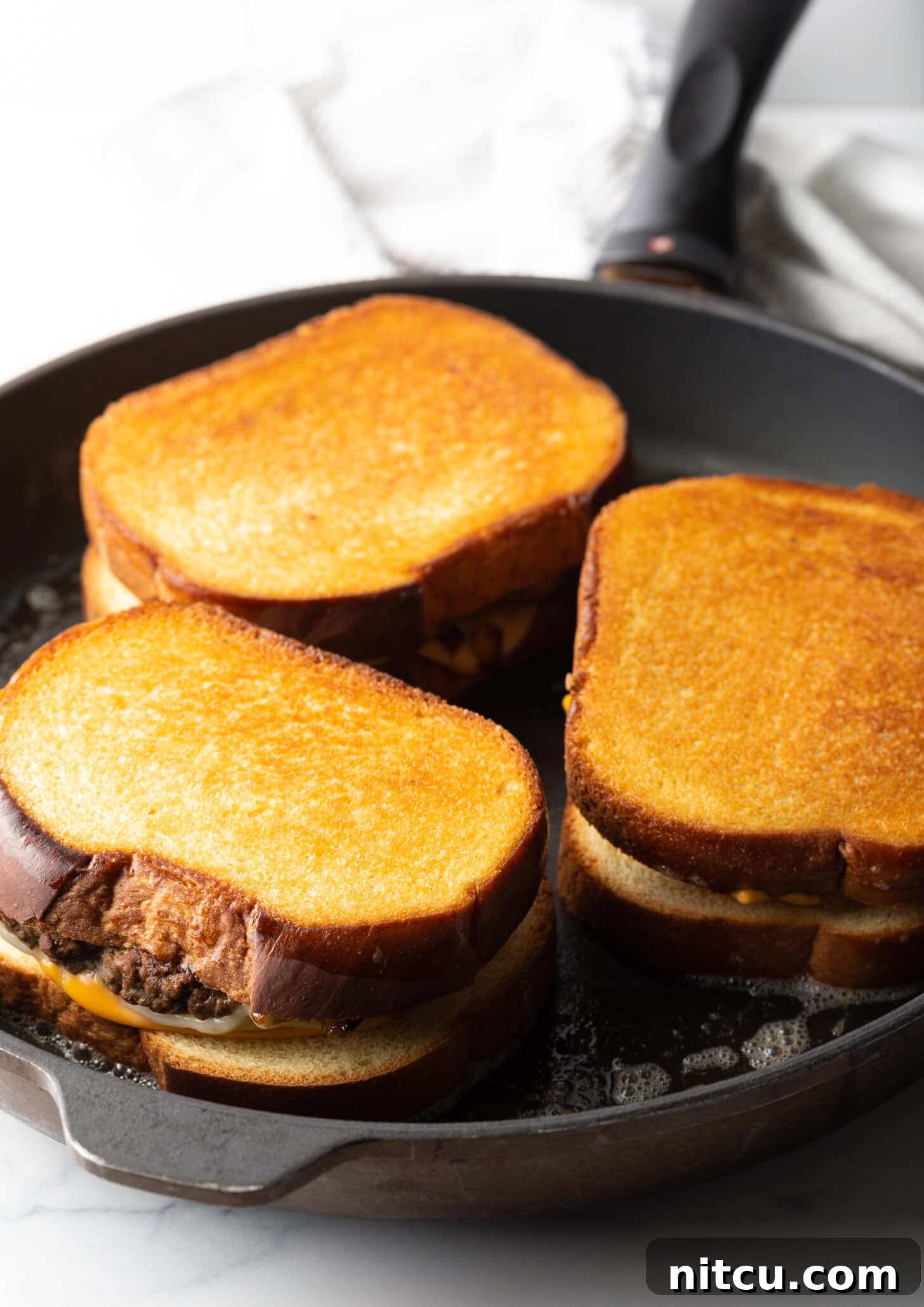 Three sandwiches being toasted in a large skillet.