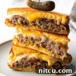 Three pieces of two patty melts stacked on top of each other. A wood skewer with small pickle is going through the top of the sandwich stack.