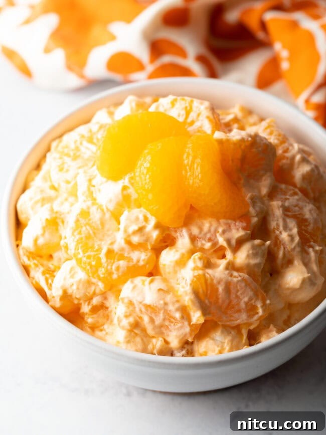 Top down view of orange fluff salad recipe in a white bowl, garnished with 3 slices of oranges.