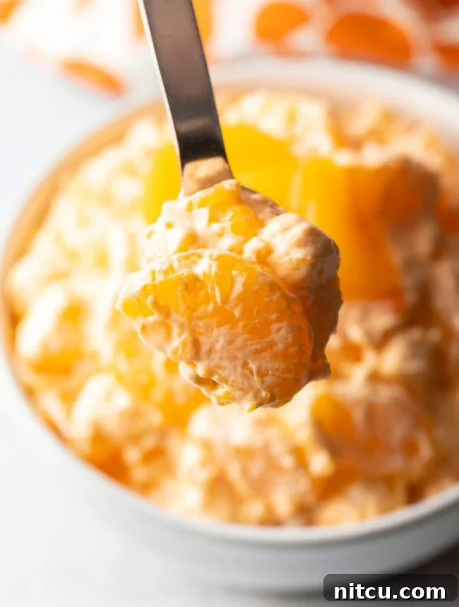 Spoon showing creamsicle fluff salad to camera.