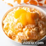 Top down view of mandarin orange fluff salad in a white bowl, garnished with 3 slices of oranges.