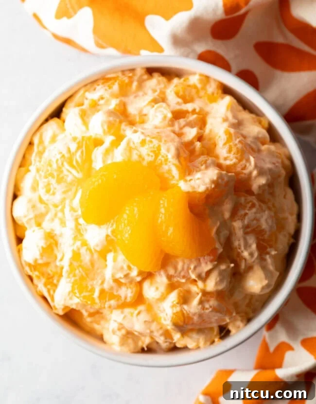 Top down view of mandarin orange salad in a white bowl, garnished with 3 slices of oranges.