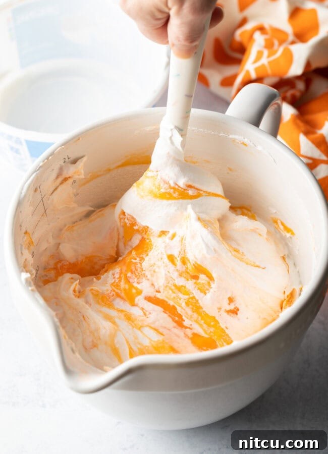 White bowl, orange fluff being mixed by white spatula.