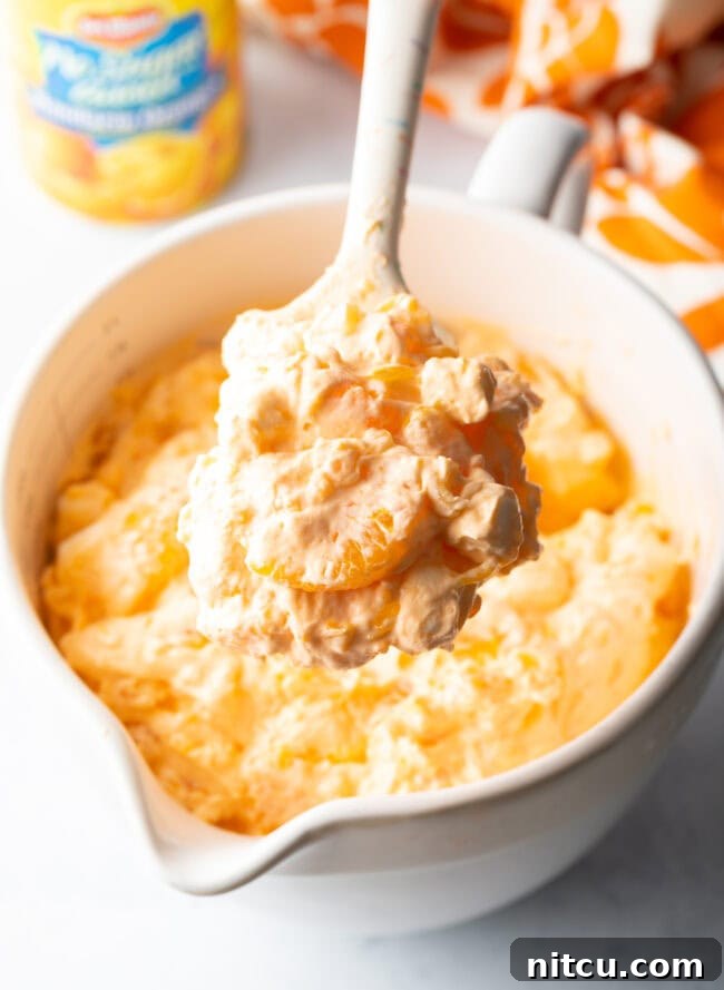 Spoon showing creamsicle fluff salad to camera.