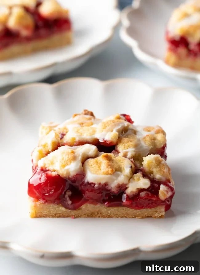 A perfectly square piece of homemade cherry pie bar, showcasing its vibrant red filling and golden crust, resting elegantly on a white scalloped plate.