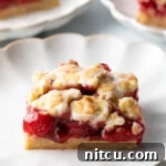 Square piece of cherry pie bar on a white scalloped plate.