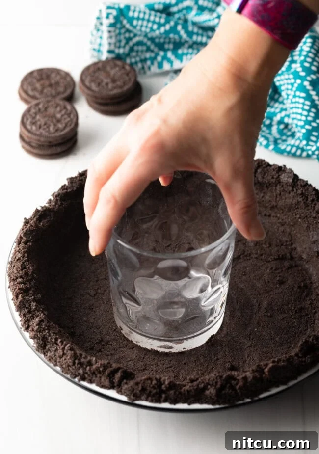 Oreo crust being pressed into a pie pan.