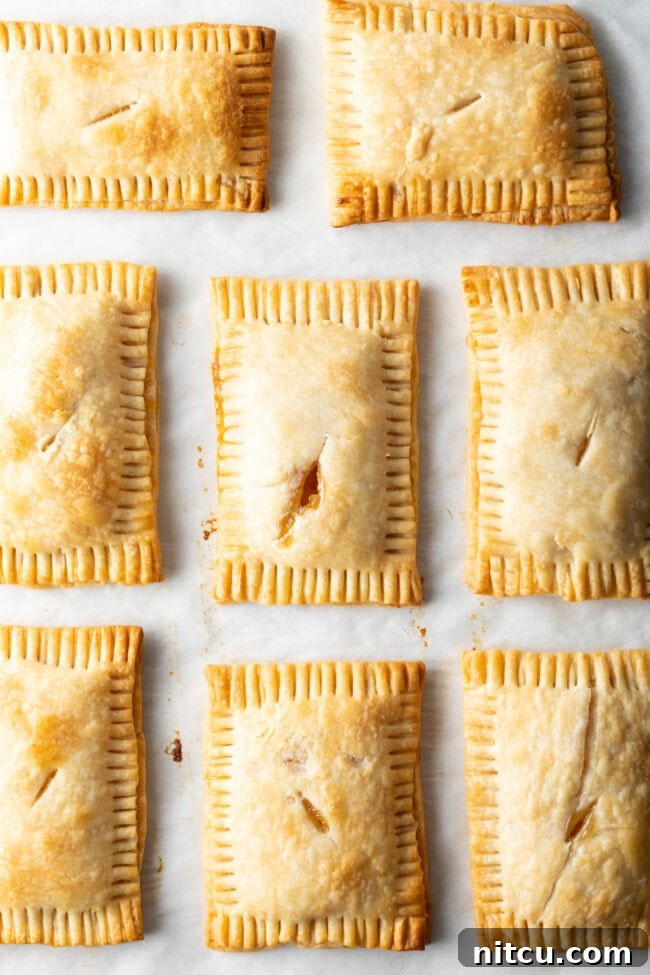 Top-down view of eight golden-brown, baked hand pies, fresh out of the oven and cooling on a parchment-lined baking sheet.