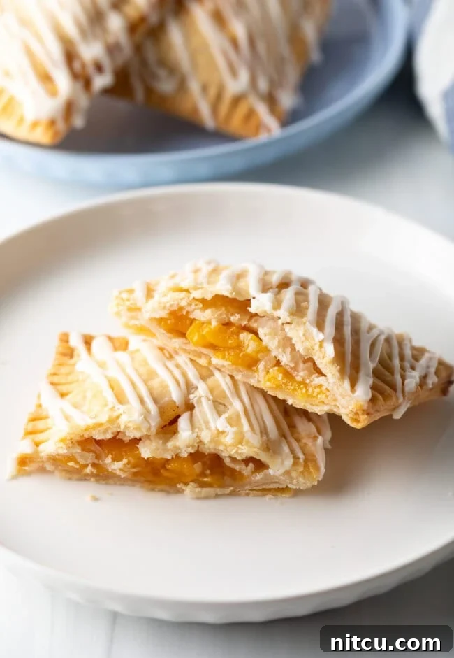 A perfectly baked peach pop tart on a white plate, expertly cut in half to showcase its enticing peach filling. One half is gently resting on the other.