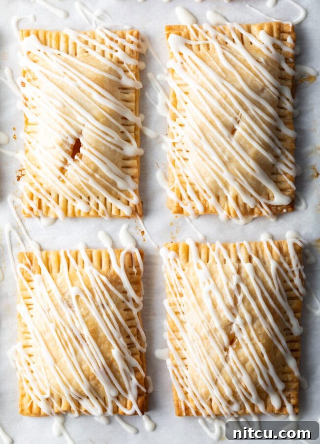 Top-down view of four finished peach hand pies, beautifully arranged on a white surface, each drizzled with sweet white icing.
