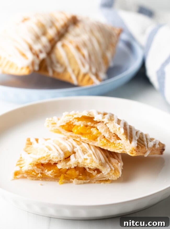 A perfectly baked peach pop tart on a white plate, cut in half to beautifully expose the warm, golden peach filling. One half rests gently on the other.