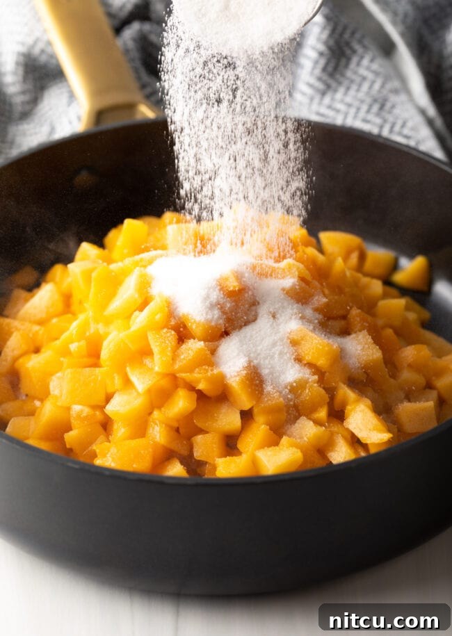 Adding granulated sugar to fresh chopped peaches in a large black pot on the stovetop, ready for cooking.