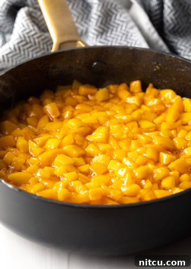 Peach mixture gently simmering in a large pot on the stovetop, thickening into a delicious jam-like filling.