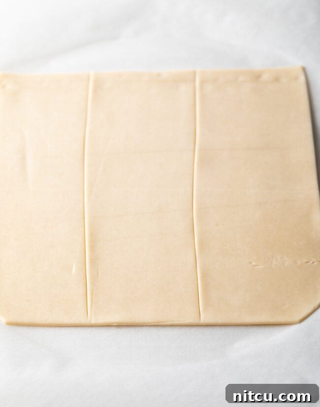A rolled-out pie pastry sheet neatly cut into three equal rectangular sections lengthwise, ready for filling.